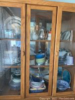 Full cabinet view showing plates, bowls, cups, and large serving pitchers and trays.