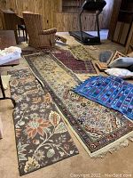 Overview photo showing multiple rugs and runners in various patterns and colors laid out on floor.