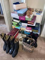 Pile of stacked shoe boxes in various colors and brands plus pairs of boots and shoes on the floor and in a tote bag