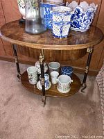 Full view of the oval wooden side table with decorative metal legs and multiple ceramic cups and planters placed on top and on the lower shelf.