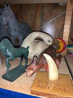 Carved wooden horse and green metal ram sculptures on shelf with wooden background