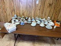 Full display of all tea cups and saucers arranged on a table showing quantity and variety of the lot.