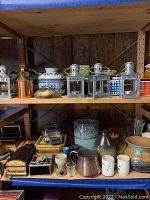 Wide view of shelf showing metal lanterns, ceramic vases, copper cup, small bowls, jewelry boxes, and metal car.