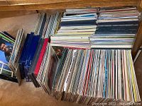 Photo of a large wooden box filled with over 100 vinyl records stacked vertically and horizontally, showing many different record spines.