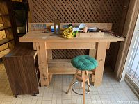 Full view of wooden workbench with tools on top, adjustable stool in front, and wooden cabinet on wheels to the side