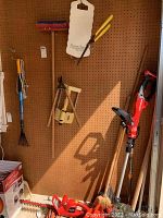 Photo showing Craftsman weedeater, Hedger trimmer, and various yard tools hanging on pegboard including rakes, broom, and clippers.