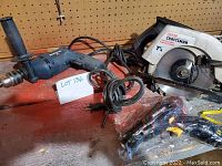 Photo of two drills and one circular saw on workbench showing cords and pegboard background