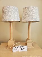 Pair of wooden table lamps side by side with white floral shades, plugged in and placed on wooden surface