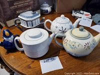 Five teapots displayed on wooden table, showing variety of colors and shapes