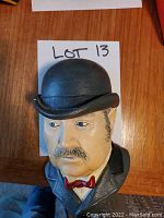 Photo showing Bosson chalkware head bust of Dr. Watson wearing bowler hat and red bow tie on wooden surface with Lot 13 paper.