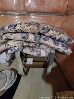 Stack of 4 floral cushions placed on one white plastic chair.