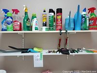 Overview of cleaning products, various spray bottles, liquid cans, and blue dustpans set on a white shelf.