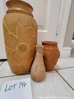 Three Cuban pottery vases with embossed floral pattern, arranged on tiled floor.