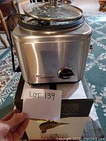 Cuisinart stainless steel rice cooker and steamer sitting on its box with a handwritten lot number in front.