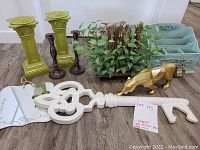 Wide shot of all decor items showing mail holder, two green candle pedestals, two dark taper holders, greenery arrangement, large white skeleton key and golden jaguar figurine.