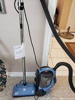 Full view of the blue Dirt Devil vacuum cleaner standing upright with attached metal handle and hose.