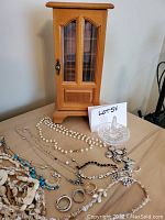 Wooden jewelry box and assortment of costume jewelry laid out on table including necklaces, rings, and glass ring dish.
