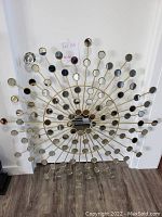 Overview photo showing the large starburst metal wall sculpture with circular mirrored elements, standing on the floor against a white wall.