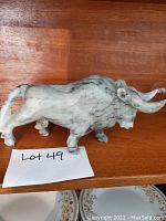 Side view of the onyx bull sculpture placed on a wooden shelf with a lot number card in front.