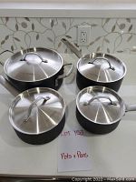 Set of four black pots and pans with stainless steel lids on a countertop, showing the group as a full set.