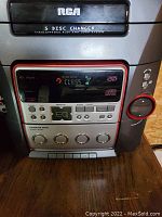 Close-up of RCA stereo main unit showing 5 disc changer slot, control buttons, digital display, and tuning dial with red trim.