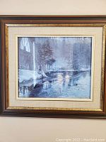 Framed print of a snowy forest and river scene with wooden frame and gold trim