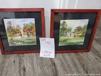 Two framed prints side by side showing South African village scenes with huts and people