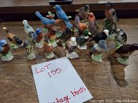 Group photo of 14 vintage ceramic bird figurines arranged on a wooden surface, showing a variety of species, colors, and positions.
