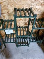 Full view of the green wooden tiered plant stand with multiple slatted shelves, showing overall structure and condition.