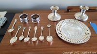 Overview of all items: 2 candle holders, 2 napkin rings, 1 Birks spoon, 6 collector spoons, and glass dish with pierced tray