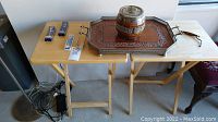 Full view of lot showing two natural wood folding TV trays with small boxed collector spoons on one, large wooden serving tray with dark metal carved inset and metal handles, and wooden biscuit tin with metal top and handle labeled 'BISCUITS'.