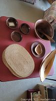 Photo showing large burl wood salad bowl, smaller wood bowls, a pair of wooden salad servers, an oblong wooden bowl, and woven placemats on a table.