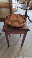 Copper flower-shaped bowl on top of wooden side table.