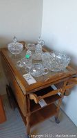 Photo of the complete set of crystal glassware displayed on a wooden rolling cart showing all items including the fruit bowl, oil bottle, creamer, sugar dish, olive dish, salt pot, and candy dish.