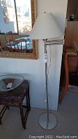 Full view of the brushed nickel pivot arm floor lamp standing next to wooden furniture and a decorative mirror, showing its height and design.