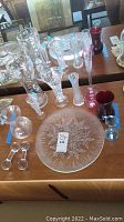 Photo showing assortment of clear crystal vases, colored glass vases, glass cream pitcher, glass snowflake dish, and cutlery holders on wooden surface