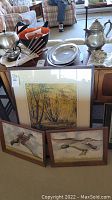 Two matching framed duck paintings alongside one signed watercolor landscape painting below them on floor.