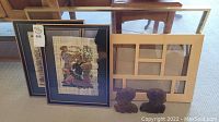 Photo showing two framed papyrus paintings, wooden multi-opening frame, and carved elephant bookends on floor
