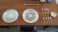 View of all items including two silver plated trays, silver plated Birks dish, four silver spoons (Community Ballad design) and four smaller spoons arranged on a table.