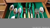 Drawer containing an assortment of silver plated flatware including serving spoons, forks, and Birks carving set with cream-colored handles