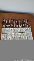 Overview of rolled-out cloth displaying approximately 24 collector spoons in two rows