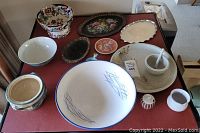 Full view of assortment of stoneware and ceramic dishes, bowls, platters, mortar and pestle on a red surface