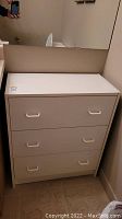 Front view of white three-drawer storage cupboard showing all drawer handles and scratches on surface.