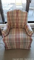 Front view of the upholstered armchair showing plaid fabric, padded arms, and skirted base.