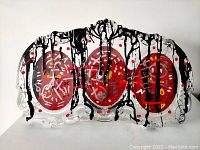 Front view of the clear acrylic sculpture featuring three red circular motifs and black paint drips