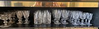 Full collection of 22 vintage crystal glasses in pinwheel pattern arranged in a row on a shelf.