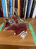 Photo showing all five art glass figurines on a wooden surface with books in background. Includes clear swan, small rabbit, reddish-brown animal, and two speckled birds.