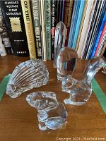 Four clear lead crystal animal figurines displayed on wood surface with books in background, showing pelican, porcupine, squirrel, and rabbit figurines.