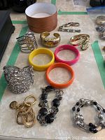 Photo showing various bracelets, gold and silver-tone bangles, colorful plastic vintage bangles, and brown jewellery box.