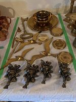 Overview photo showing brass decorative birds, plaques, plates, gavel, and other items spread on a white cloth.